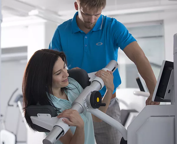 Vrouw doet oefening op Samcon biomedical equipment met begeleiding van fysiotherapeut, revalidatietraject ondersteund door SDM Smart Deal.