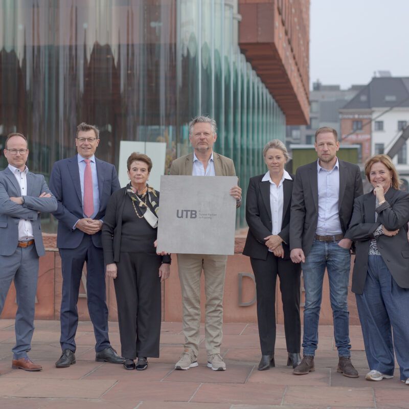 Group photo of eight members of the UTB and RG Tegel management teams in front of the MAS in Antwerp, marking their strategic merger via a Smart Deal.